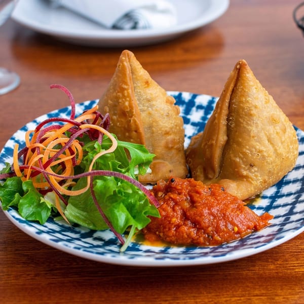 Two golden-brown samosas with a side of red chutney and a fresh green salad.