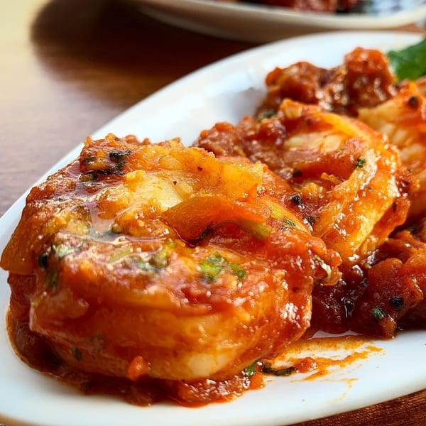 Close-up of Indian shrimp curry, featuring plump shrimp in a rich, reddish-orange sauce with herbs.