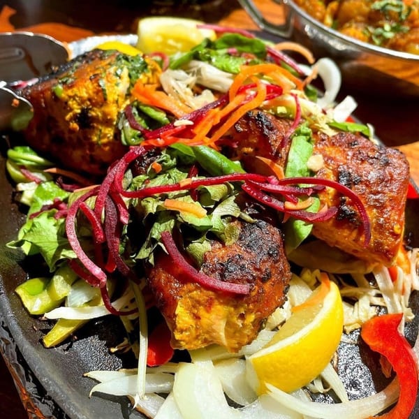 Indian chicken tikka, garnished with fresh salad, lemon, and onions, served on a hot plate.