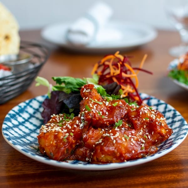 Spicy Indian chicken wings with sesame seeds, green onions, and a side salad on a patterned plate.